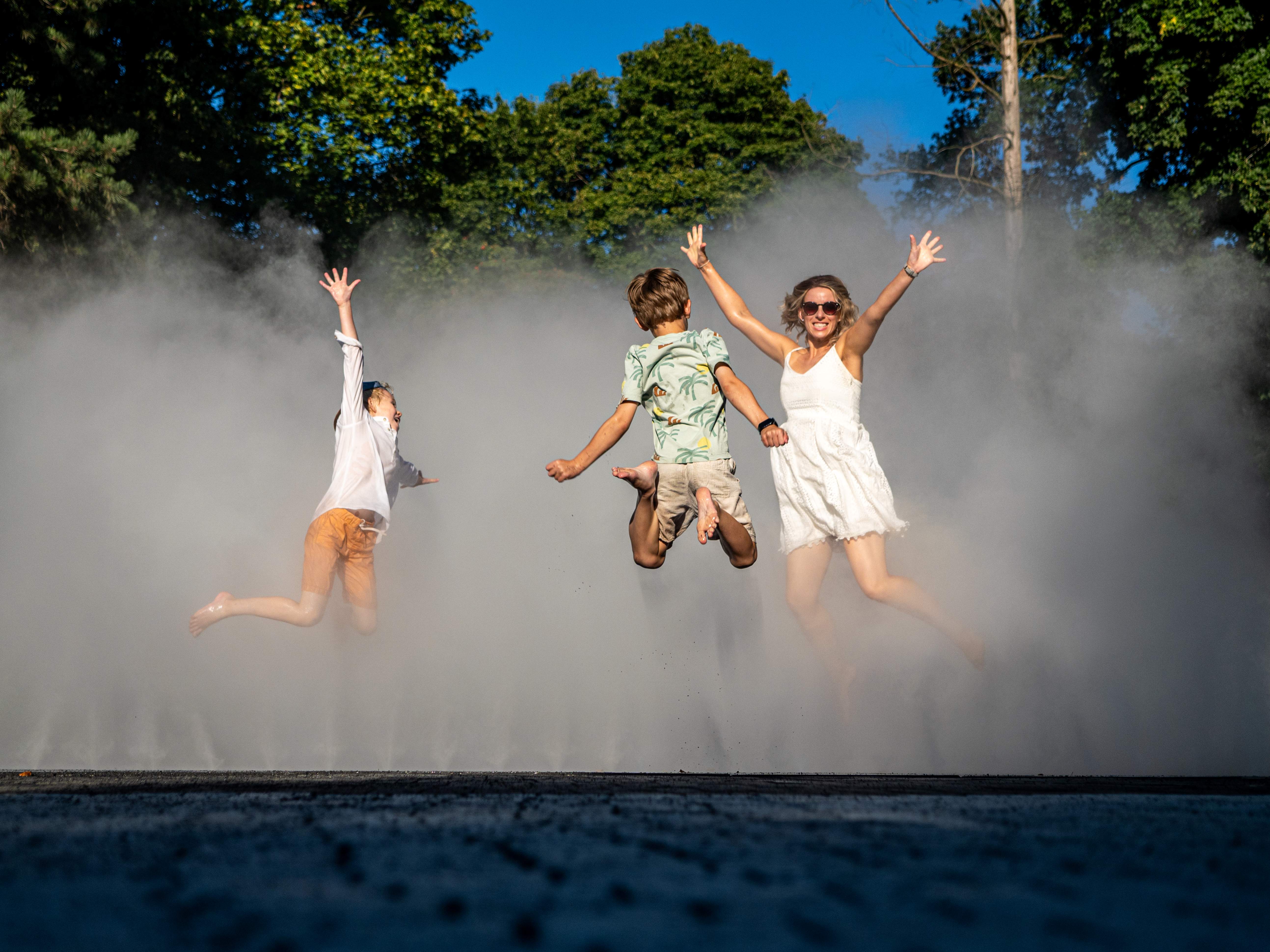 Eine Frau und zwei Kinder springen mit Freude im dichten Nebel der Sparkassen Auenlandschaft