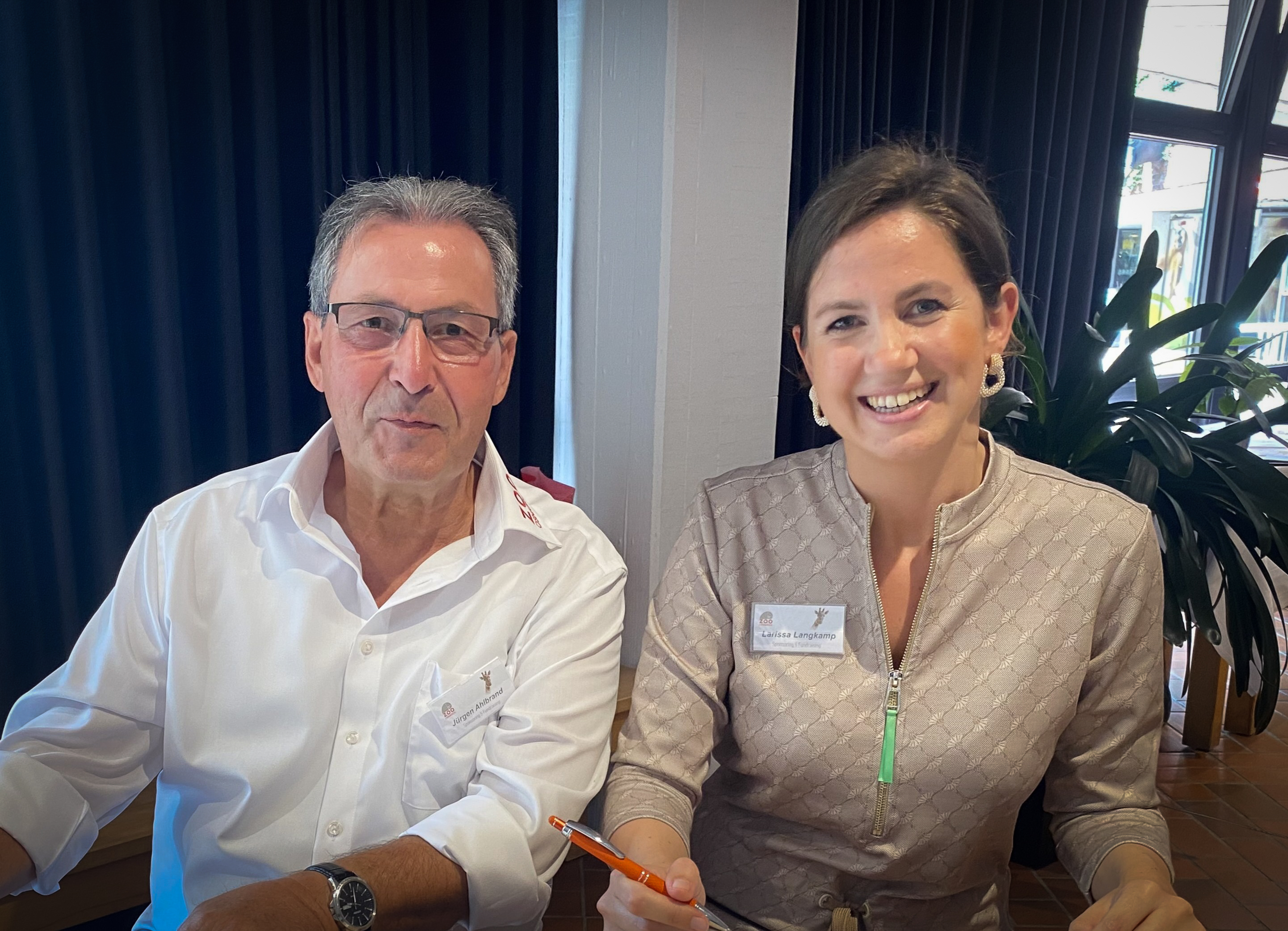 Ein Herr und eine Dame sitzen an einem Tisch und begrüßen Gäste einer Veranstaltung des Zoo Osnabrück