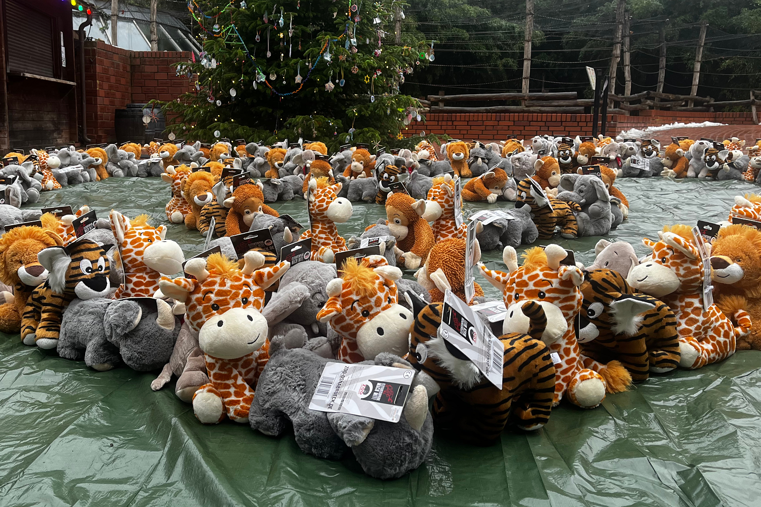 Viele Plüschtiere Giraffen, Tiger, Elefanten liegen auf einer Plane vor einem Baum.
