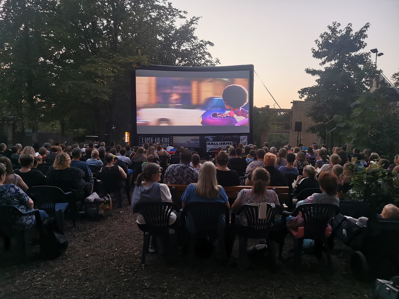 Menschen schauen bei Sonnenuntergang einen Animationsfilm auf einer Leinwand.