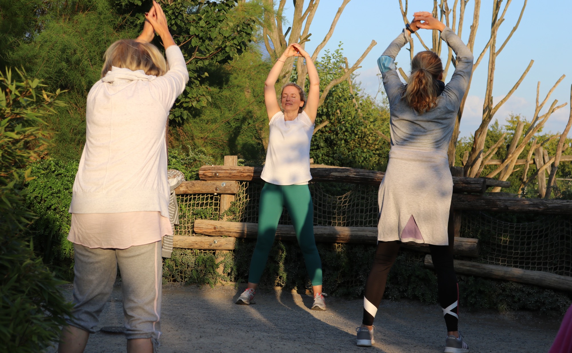 Drei Frauen machen Gymnastik im Freien und strecken die Arme nach oben.