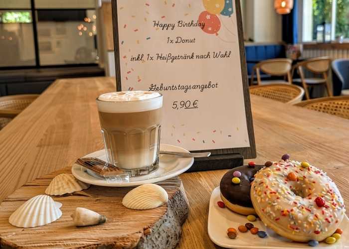 Jubiläumsmenü mit Kaffee und Donut mit bunten Streuseln auf einem festlich dekorierten Tisch
